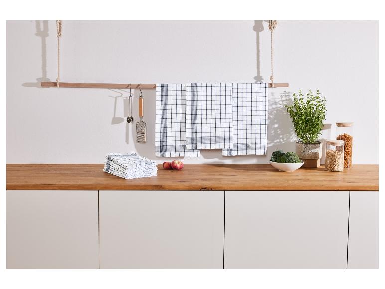 Serviettes de cuisine à carreaux bleus, suspendues à une barre en bois.