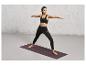 Une femme en tenue de sport noire fait du yoga sur un tapis violet de Jette Sport.