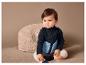 Un bébé vêtu d'une veste en polaire bleu et noir assis sur une couverture beige.