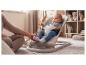 Bébé dans un transat, avec la main d'un adulte touchant le pied du bébé, sur un tapis moelleux.