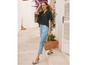 Une femme porte un chemisier noir, un pantalon bleu et des sandales tout en tenant un sac en osier.