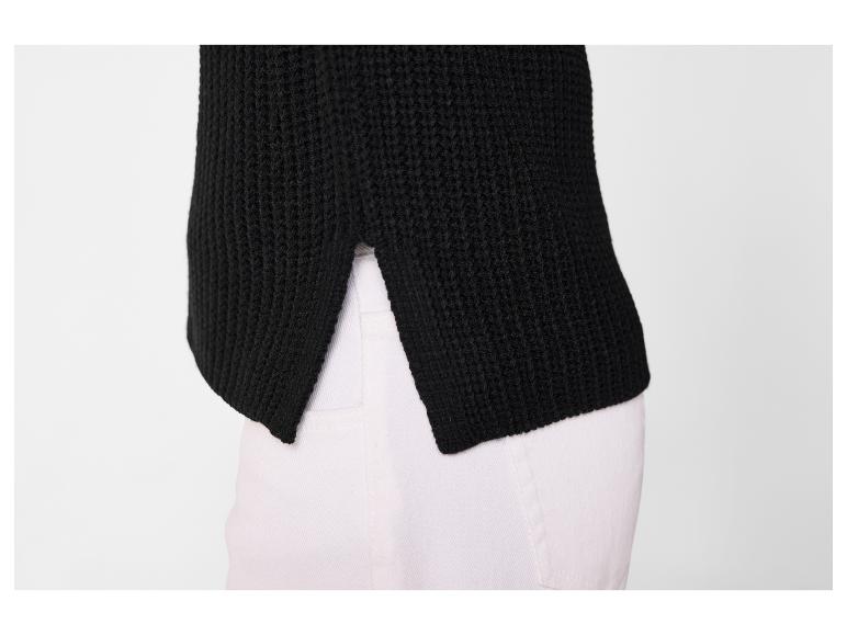 Pull en maille noir avec fentes latérales, porté sur un pantalon blanc.