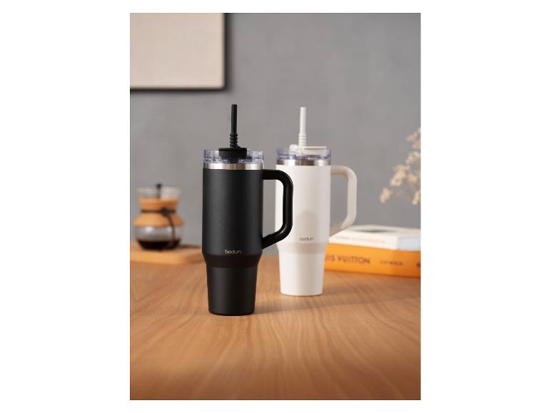 Deux tasses de voyage Bodum, une noire et une blanche, avec pailles sur une table en bois.
