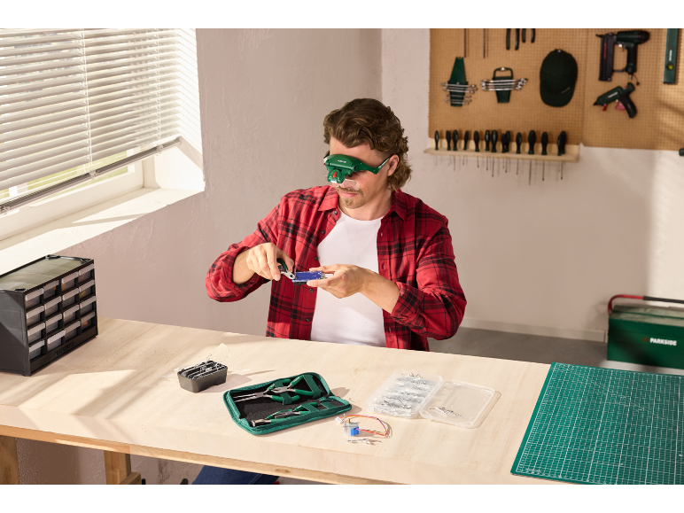 Homme avec une loupe frontale réparant de l'électronique sur un établi.