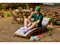 Homme en bob et ensemble verts, assis sur une chaise longue mangeant de la pastèque.