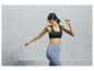 Une femme porte un soutien-gorge de sport noir et un legging bleu.