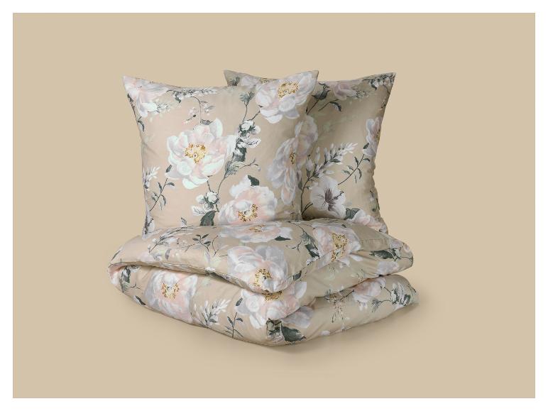 Parure de lit florale avec deux oreillers et une couette pliée, ornée de grandes fleurs blanches et roses sur fond beige.