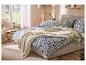 Chambre avec lit, couette bleue à motifs, plaid beige et chaise en bois.