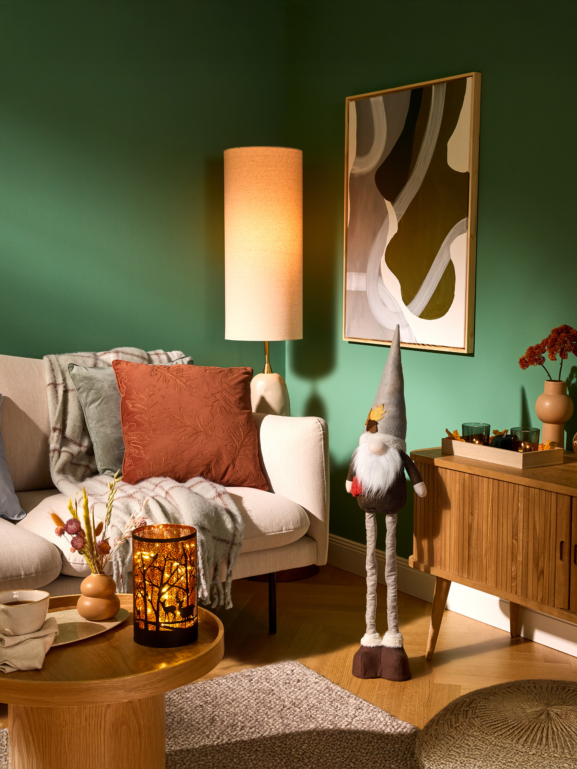 Salon confortable avec murs verts, canapé, lampadaire et décorations d'automne.