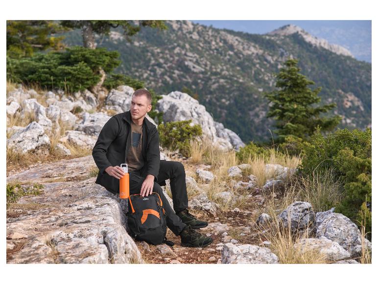Homme assis sur un rocher avec un sac à dos et une bouteille d'eau, montagnes en arrière-plan.