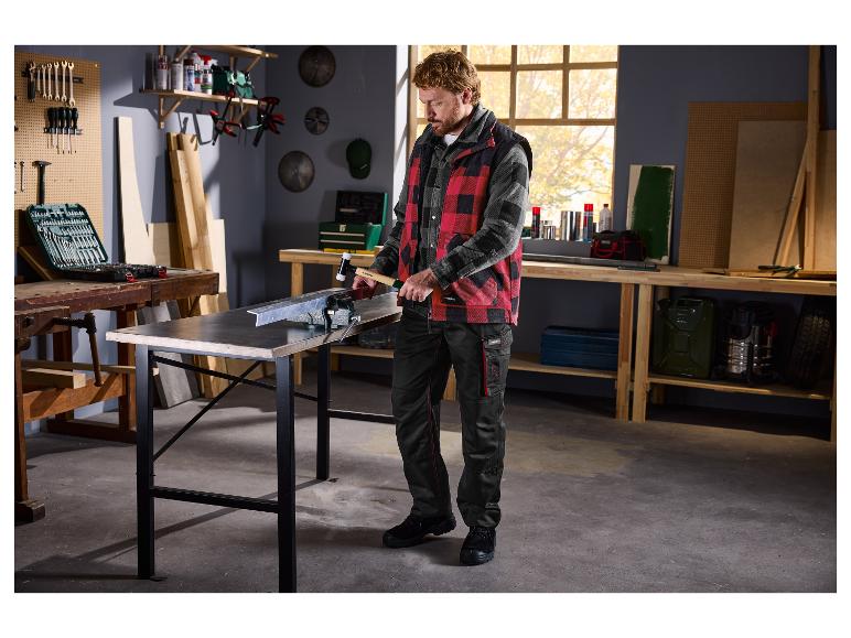 Homme en tenue de travail martelant une pièce de métal dans un atelier.