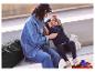 Une mère et sa fille sont assises sur un banc avec une valise noire et une valise pour enfant.