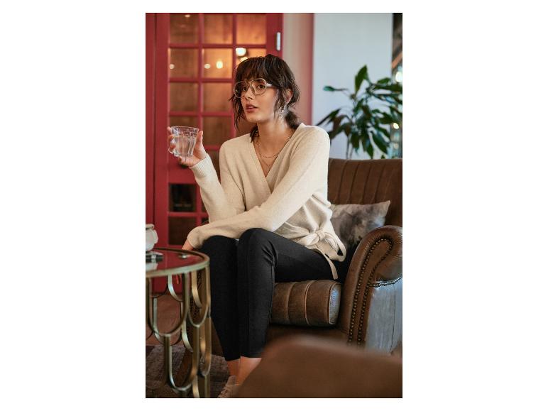Une femme vêtue d'un pull beige et d'un pantalon noir est assise dans un fauteuil en cuir.