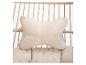 Coussin beige avec texte brodé 'HOME DELUXE', attaché à une chaise suspendue.