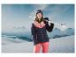 Une femme en tenue de ski pose avec des skis sur une montagne enneigée.
