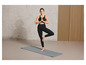 Une femme en brassière de sport noire et leggings fait du yoga sur un tapis gris.
