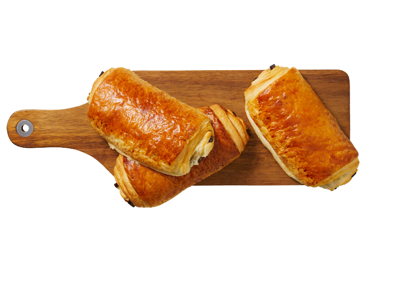 Pains au chocolat dorés sur une planche à découper en bois.
