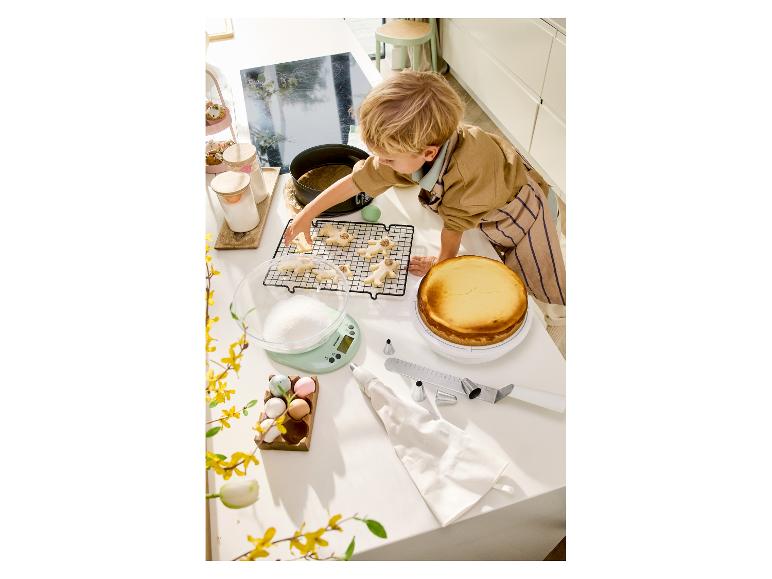 Enfant décorant des biscuits et un cheesecake sur un comptoir de cuisine avec des outils de pâtisserie.