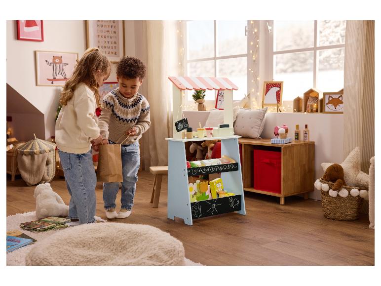 Deux enfants jouent avec un stand de marché jouet dans une pièce festive.