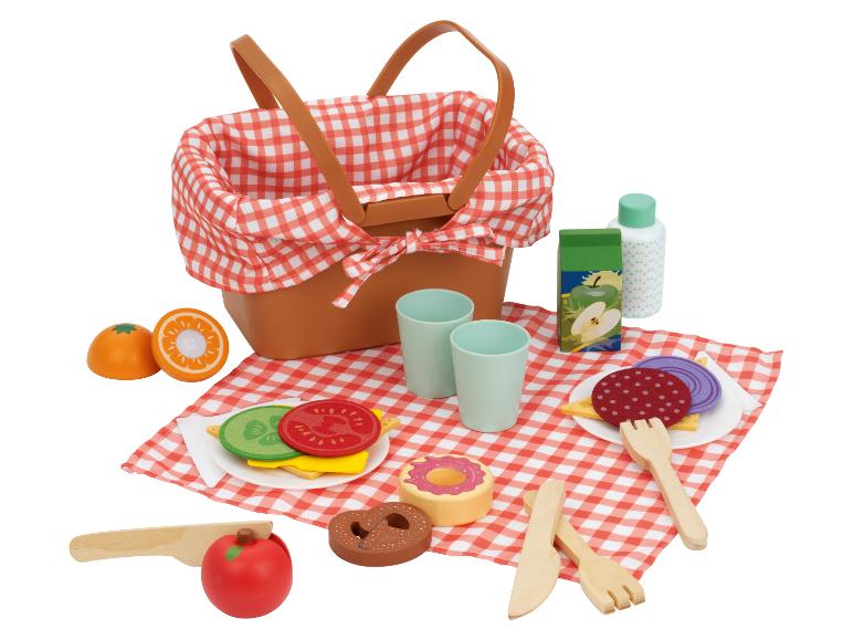 Ensemble de pique-nique avec panier, couverture à carreaux, sandwichs, fruits, boissons et couverts.