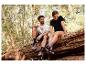 Couple en t-shirts et chaussures de sport assis sur un tronc d'arbre en forêt.