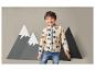 Un garçon portant une veste beige à motif d'arbres et un jean devant un fond de montagne.