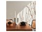 Table en bois avec bougie, tasse, bol et branches bourgeonnantes au soleil.