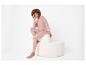 Femme souriante en ensemble loungewear rose, assise sur un pouf blanc.