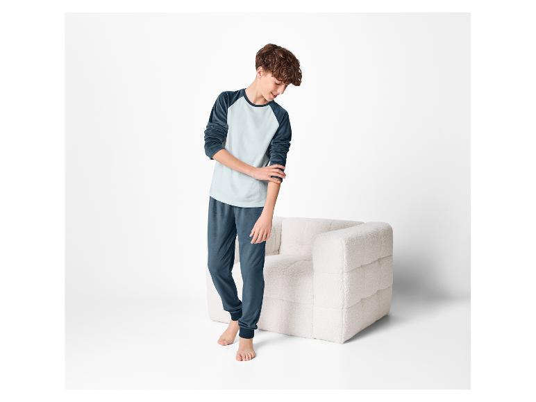 Un garçon en pyjama confortable, debout à côté d'un fauteuil moelleux.