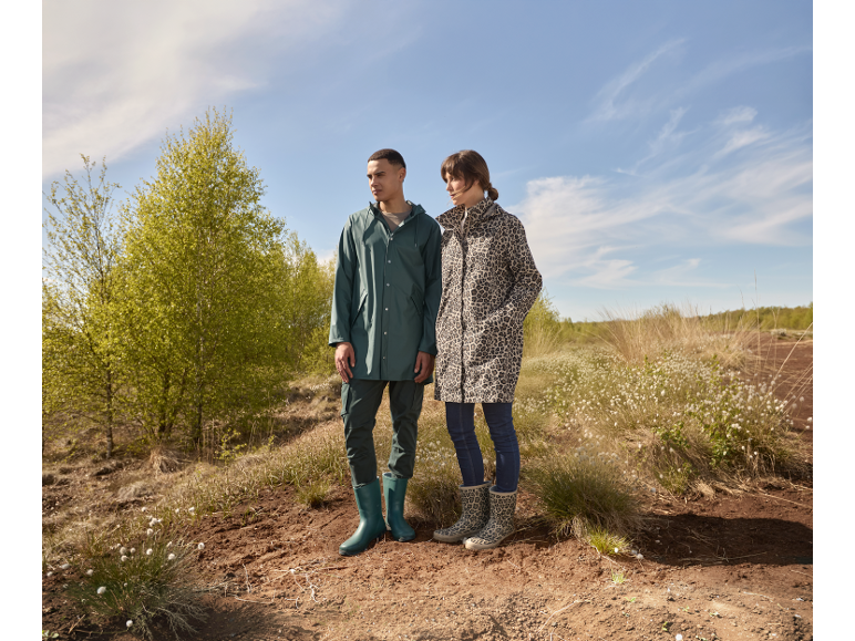 Homme et femme en imperméables et bottes dans la nature.