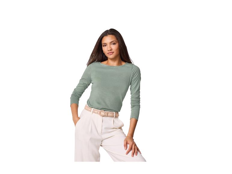 Femme portant un haut vert à manches longues et un pantalon blanc avec une ceinture tressée.