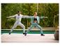 Un homme en veste de jogging grise CRIVIT et une femme faisant du yoga au bord de la piscine.