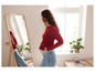 Une femme en pull rouge et jean bleu se regarde dans un miroir.