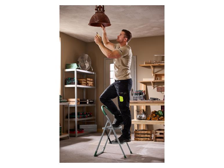 Homme sur échelle changeant ampoule de plafonnier dans un atelier.