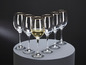 Six verres à vin avec un bord doré, dont un rempli de vin blanc.