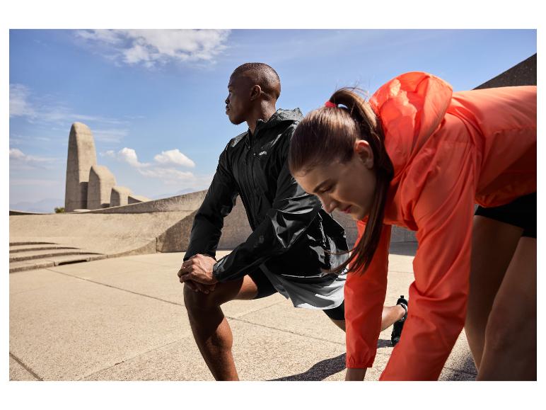 Deux athlètes en tenue de sport s'étirent en extérieur, avec un monument en arrière-plan.