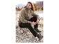 Homme en veste polaire marron et pantalon noir assis sur des rochers.