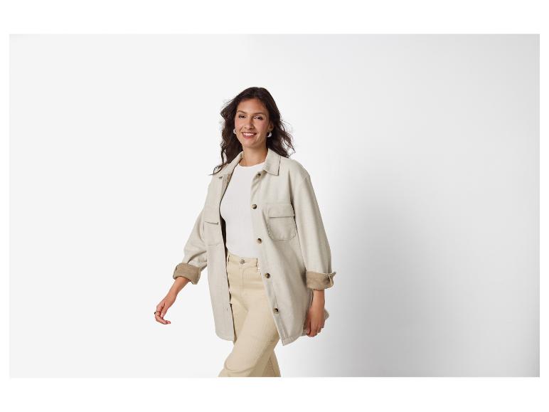 Femme en surchemise et pantalon beiges, souriante sur fond blanc.