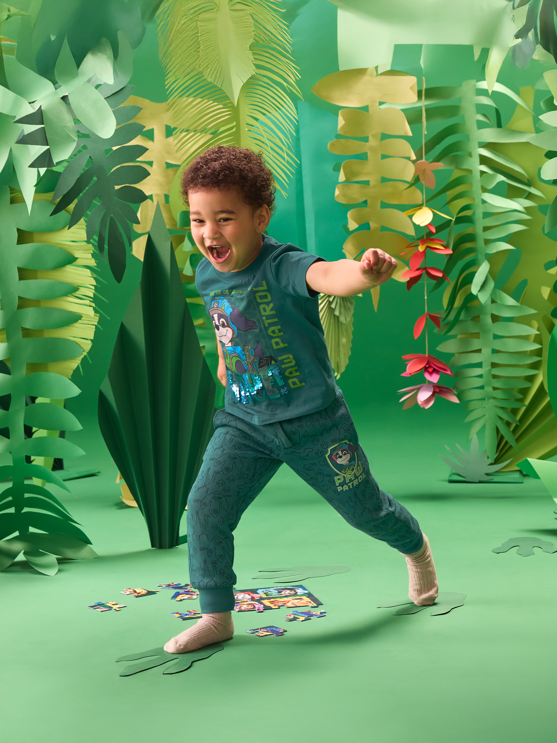 Petit garçon en t-shirt et jogging verts thème jungle, jouant avec un puzzle.