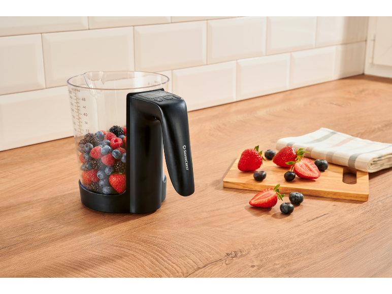 Pichet de mixeur rempli de baies sur un comptoir de cuisine, avec des fraises coupées à côté.