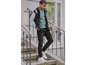 Un jeune homme en veste varsity, jean et baskets avec une planche à roulettes à la main.