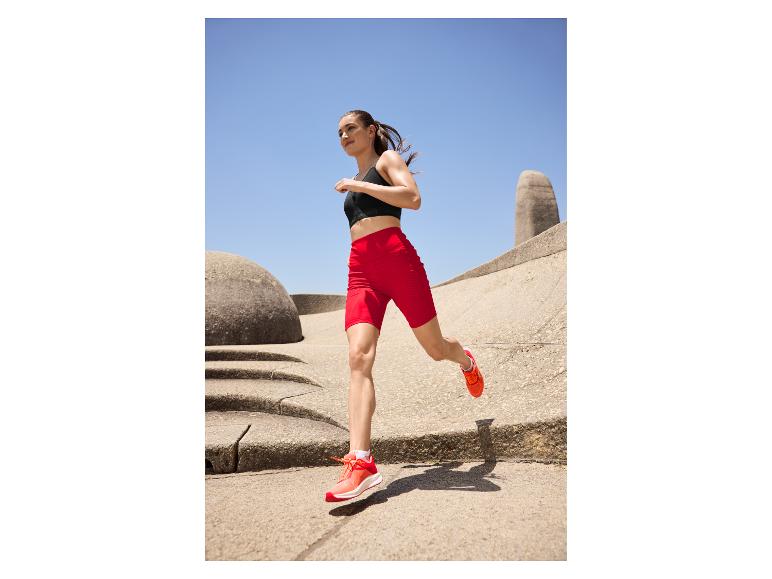 Femme en brassière de sport noire et short cycliste rouge courant en extérieur.