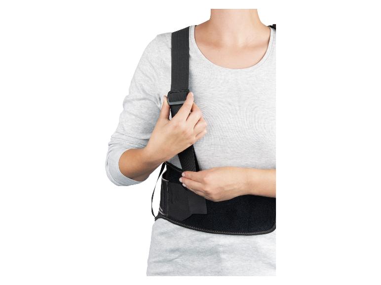 Femme ajustant un correcteur de posture ou une ceinture lombaire noire sur un t-shirt gris à manches longues.