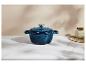 Cocotte en fonte bleue avec couvercle sur une surface en marbre blanc, avec un pot en arrière-plan.