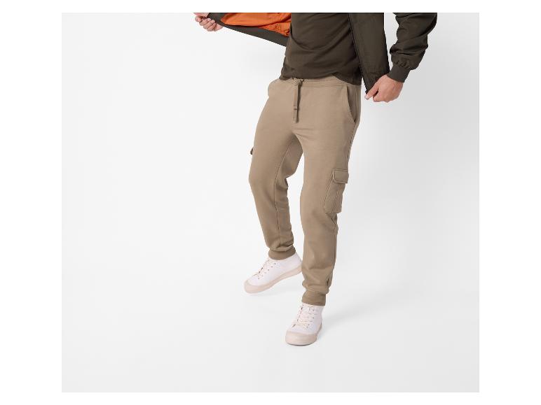 Homme portant un pantalon cargo marron, un t-shirt vert foncé et une veste doublée orange.