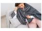 Une femme assise sur un canapé gris avec une couverture électrique grise.