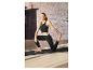 Une femme portant un legging noir et un soutien-gorge de sport s'étire sur un tapis de yoga.