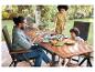 Famille profitant d'un repas en plein air avec table en bois, chaises et fruits frais.