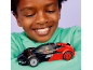 Un enfant souriant regardant une voiture jouet rouge et noire.