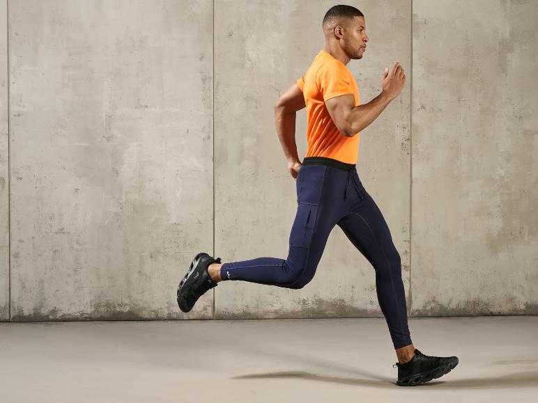 Homme courant en t-shirt orange et leggings bleus devant un mur en béton.